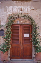 Fototapeta na wymiar Door surrounded by flowers in Boccaccio street in the ancient medieval village of Certaldo, Tuscany, Italy