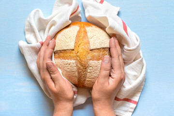 female hands holds freshly baked sourdough bread in napkin from oven on blue wooden table Top view Flat lay Homemade pastry