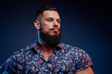 Bearded and styled handsome bodybuilder with fashionable hairstyle posing in dark blue background.