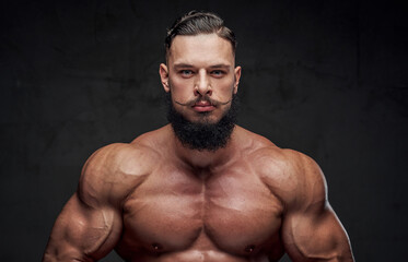 Fototapeta na wymiar Handsome bearded bodybuilder with naked torso and with modern hairstyle posing in dark background.