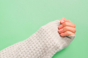 Stylish orange nails. Hand in turquoise knitted sweater on turquoise background.