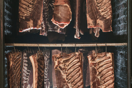 Different types of cured meats hanging in a smoke chamber