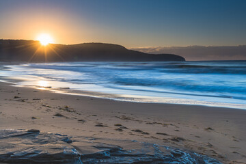 Obraz premium Clear skies winter sunrise seascape with sunburst over the headland