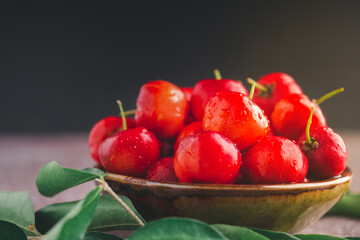 Ripe red cherries in a ceramic bowl with sunlight on black wall background