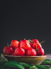 Ripe red cherries in a ceramic bowl with sunlight on black wall background