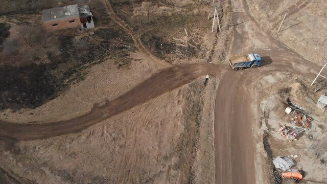 An aerial view of an empty dump truck truck driving along a dirt road. The concept of construction work and the disposal of construction waste