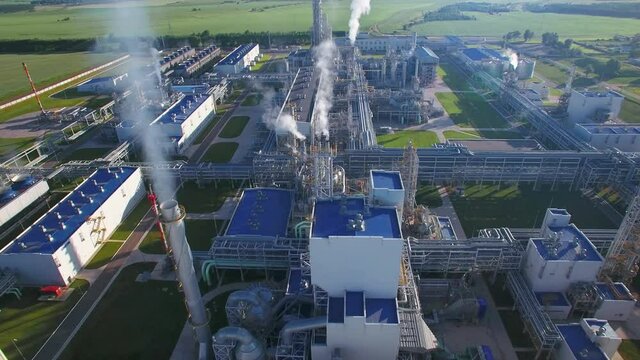 Chemical Plant produces gasoline and mineral fertilisers. Aerial flying centrally morning sunshine summer fields and grass around. Smoke smog and environmental pollution.