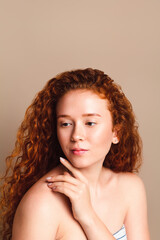 portrait of a very beautiful red-haired girl with long curly hair and cute freckles on a beige background in the studio. Retouched photo, model without makeup. Skin care concept with pigmentation