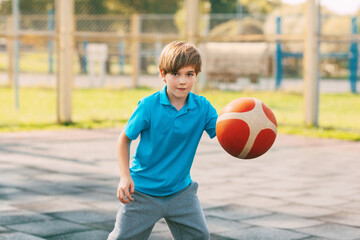 Focused cute boy athlete leads the ball in a game of basketball. A boy plays basketball after school. Sports, healthy lifestyle