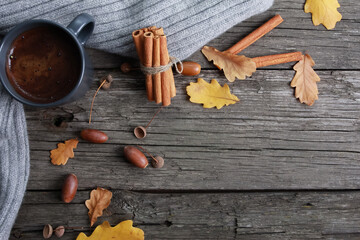 Black coffee cup, yellow oak leaves, acorns, cinnamon, grey scarf on rough old wooden boards. Copy space, top view. Autumn background, fall season, thanksgiving, coffee shop menu, hot drink concept