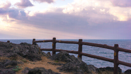 Obraz premium beautiful purple sunset over the sea, fence on the beach, purple cloudy sky, cliff over the sea, calm and peaceful concept, soft focus, film noise 