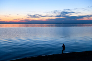 Lonely silhouette of a man standing by the sea at sunset