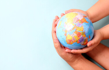 The hands holds a model globe on blue background in studio.