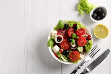 Healthy Greek salad of cherry tomato, onion, pepper, feta, black olives, basil, cucumbers, with olive oil and lemon juice on white background, Copy space