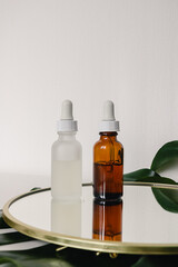 Various amber and matte glass bottles for cosmetics, natural medicine , essential oils or other liquid on a white background standing on a mirror decorated with a green monstera leaf