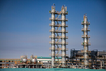Oil distillation towers on blue sky. Grey refining column on petrochemical plant. Heat exchangers and pipelines.