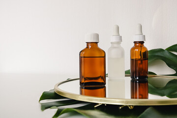 Various amber and matte glass bottles for cosmetics, natural medicine , essential oils or other liquid on a white background standing on a mirror decorated with a green monstera leaf