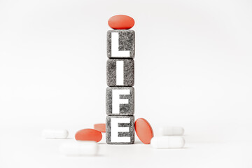 a group of white and red pills and cubes with the word life on them, white background. Concept carehealth, treatment, therapy.