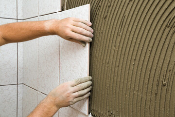 Worker hands gluing ceramic tiles on wall. Closeup. Side view.