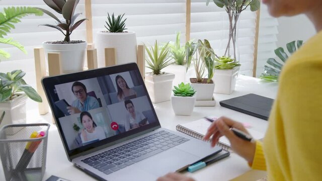 Back view of business woman talking about sale report in video conference. Asian team using laptop and tablet online meeting in video call. Working remotely green home office and Social isolation.