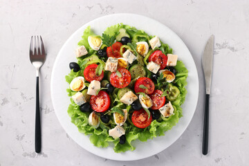 Healthy salad of cherry tomatoes, cucumbers, peppers, black olives, with olive oil, quail eggs and gorgonzolla cheese on a light background, view from above