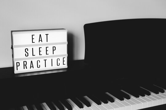 Black and white of piano keys with light box sign that reads ""EAT SLEEP PRACTICE"" - horizontal