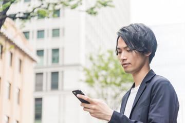 Fototapeta na wymiar オフィス街でスマートフォンを操作する若い男性