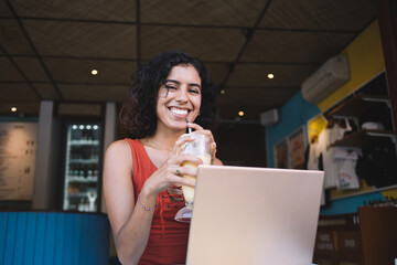 Laughing woman with laptop drinking milkshake in cafe