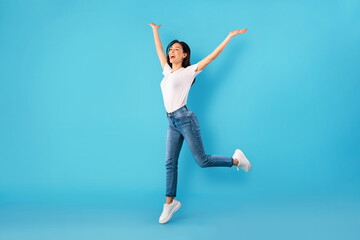 Happy woman jumping over blue studio wall