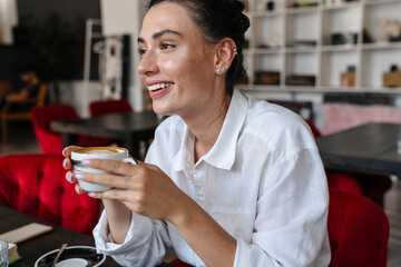Happy woman sitting indoors in cafe and drinking coffee