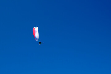 A paraglider with a motor flies in the clear blue sky.