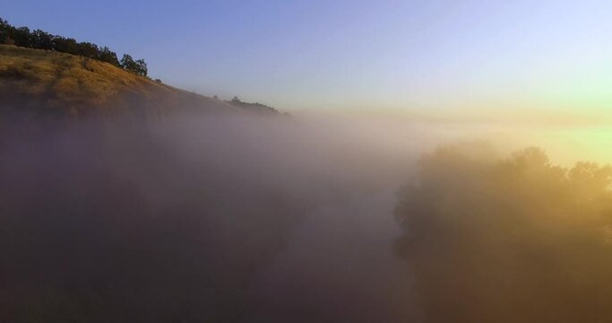 Aerial view of pink sunrise on misty valley of Siverskyi Donets river near Zmiiv city, Ukraine. Forward camera movement over riverbed