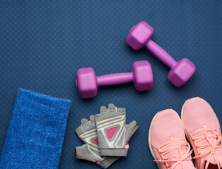 a pair of purple dumbbells, sports gloves and pink gym shoes on a blue neoprene mat