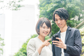 オフィス街でスマートフォンを見ながら会話する男女