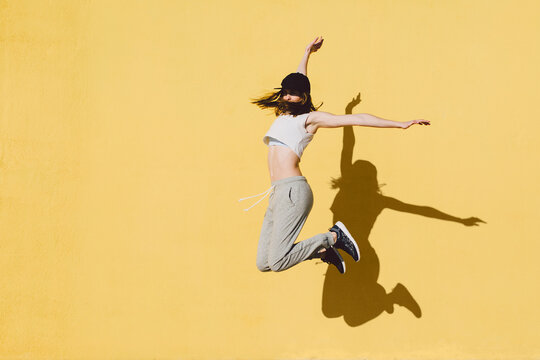 Happy woman jumping in front of a yellow wall.