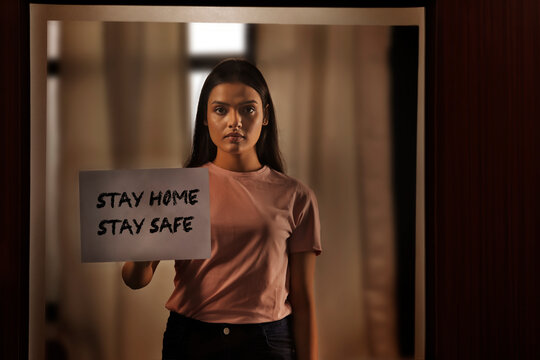 Woman holding a sign of stay at home while standing at her door