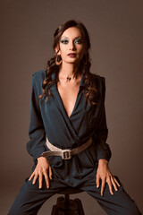 Portrait of a sexy brunette woman seated in a black stool wearing a green dress and looking at camera over a grey background