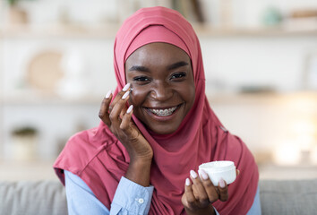 Skin Hydration. Black Muslim Woman Applying Moisturizing Cream On Face At Home