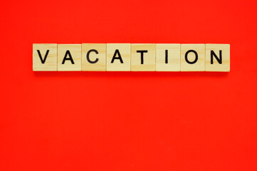 Word vacation. Wooden blocks with lettering on top of red background. Top view of wooden blocks with letters on red surface