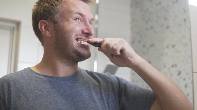 A handsome man brushes his teeth with a toothbrush in the morning in the bathroom. Reflection in the mirror