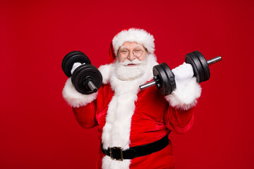 Portrait of his he nice handsome attractive cheerful cheery strong bearded Santa father wearing festal warm coat doing fit exercise isolated bright vivid shine vibrant red color background