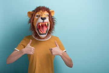 Young woman in lion mask keeps thumb up approval gesture, isolated on blue background..
