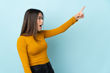 Teenager girl isolated on blue background pointing away