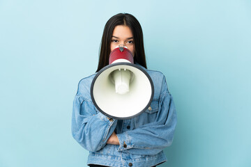 Teenager girl isolated on yellow background shouting through a megaphone to announce something