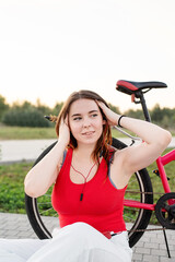Obraz premium Teenage girl sitting next to her bike listening to the music in the park at sunset