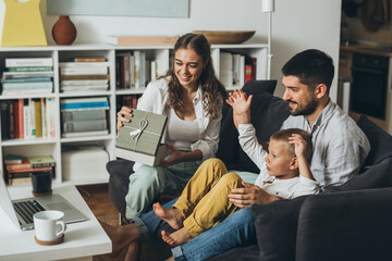 family sharing gifts and having video call on laptop computer, sitting on sofa at home