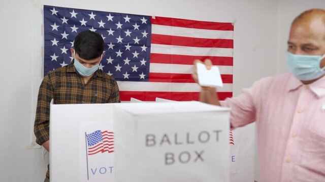 Man in medical mask placing ballot paper inside the ballot box - Concept of in person voting and people busy at polling booth at US Election