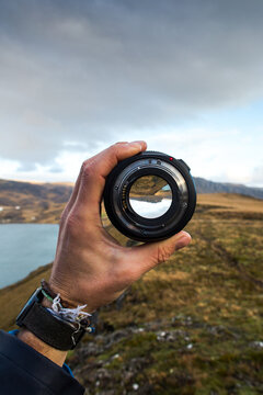 Hand holding up a camera lens and looks through it surrounded by a beautiful landscape.