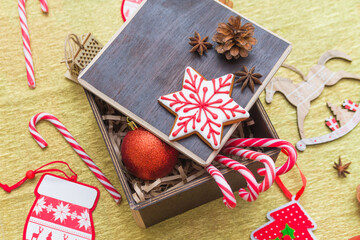 Christmas gift composition flatlay with festive decoration, gingerbread and sugar cane candies in a dark brown box on golden background. Happy New Year 2021