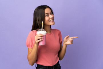Teenager girl holding a strawberry milkshake pointing finger to the side